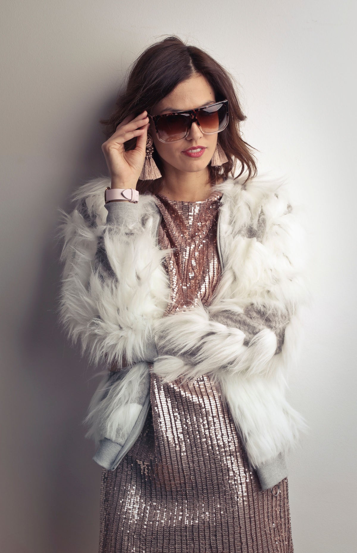 Fashionable woman in a white fur jacket and evening dress against a grey wall